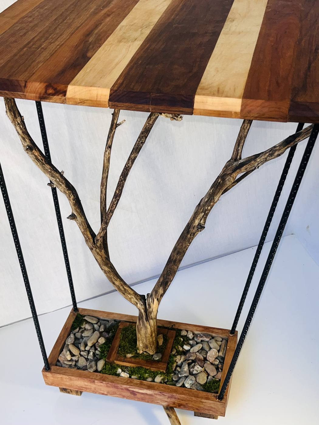 The finished console table: striped hardwood top carried on branch legs and black rebar, over a stone-and-moss tray.