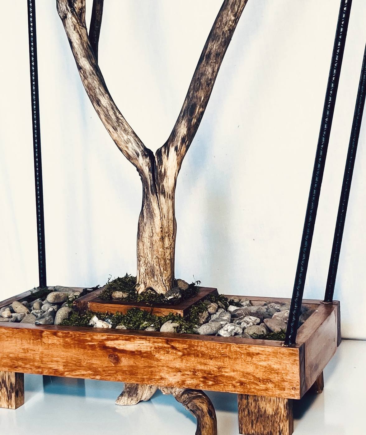 Detail of the base tray — the trunk rising from a bed of river stones and moss.